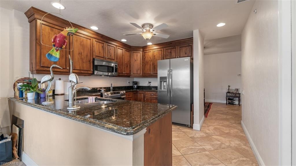 Kitchen with dark stone countertops, appliances with stainless steel finishes, a peninsula, recessed lighting, and ceiling fan