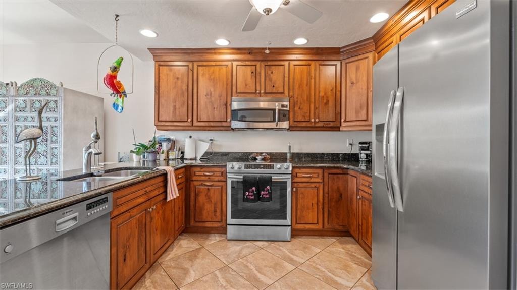 Kitchen featuring appliances with stainless steel finishes, brown cabinetry, dark stone counters, and recessed lighting