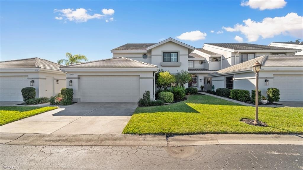 Traditional home featuring a front lawn, stucco siding, concrete driveway, an attached garage, and a tile roof