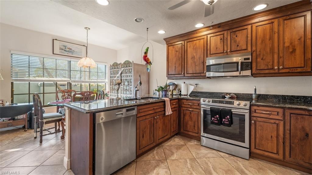 Kitchen featuring a peninsula, appliances with stainless steel finishes, dark stone counters, recessed lighting, and pendant lighting