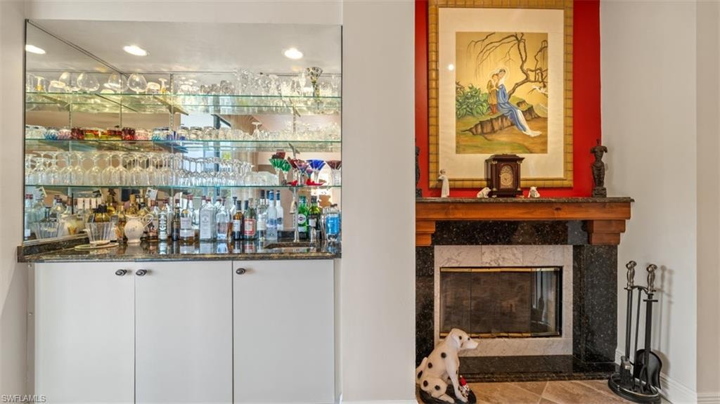 Indoor bar with white cabinets, a fireplace, dark stone counters, and recessed lighting