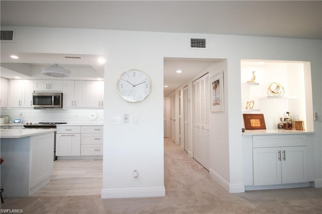 Kitchen featuring white cabinets, appliances with stainless steel finishes, recessed lighting, light colored carpet, and tasteful backsplash