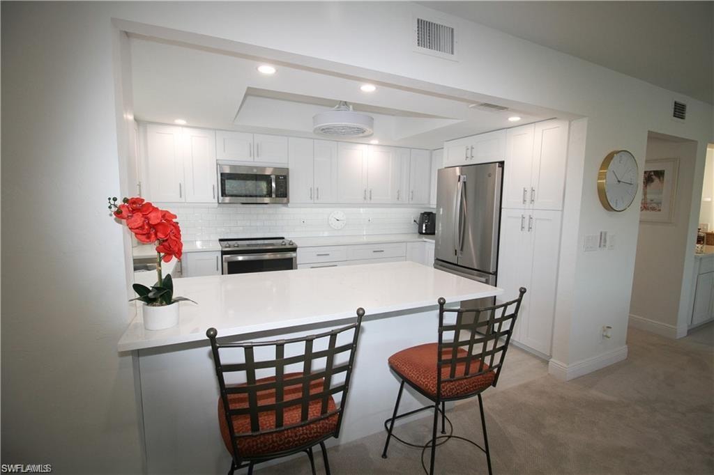 Kitchen with a breakfast bar area, a peninsula, white cabinets, appliances with stainless steel finishes, and recessed lighting