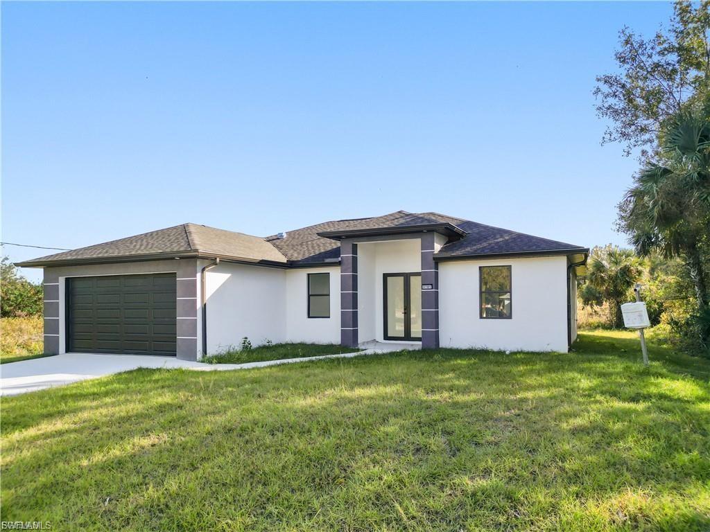 Prairie-style home with stucco siding, a front yard, an attached garage, and driveway