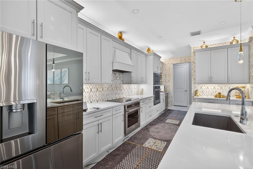 Kitchen featuring decorative light fixtures, stainless steel appliances, light stone countertops, crown molding, and premium range hood