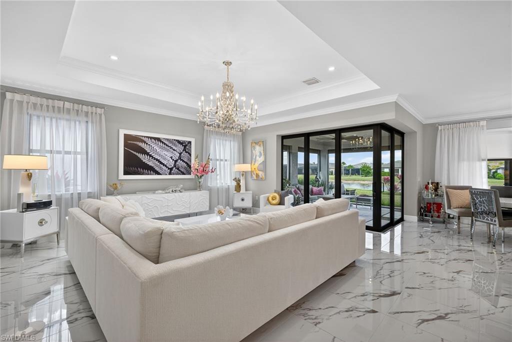 Living room with crown molding, a chandelier, light marble finish floors, and a water view