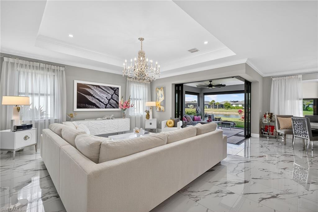 Living room with a chandelier, ceiling fan, crown molding, light marble finish flooring, and a raised ceiling