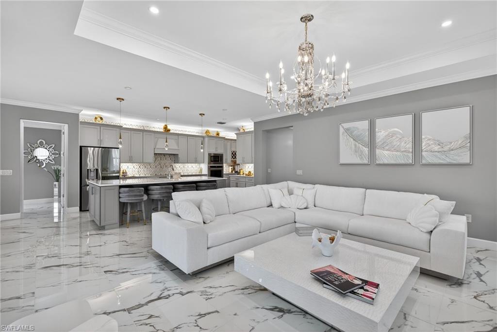 Living area with crown molding, a chandelier, a raised ceiling, and recessed lighting