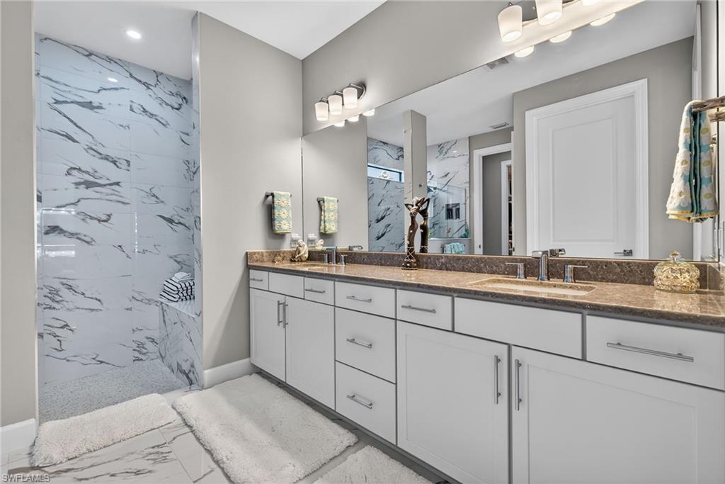 Bathroom with double vanity, a marble finish shower, light marble finish flooring, and recessed lighting
