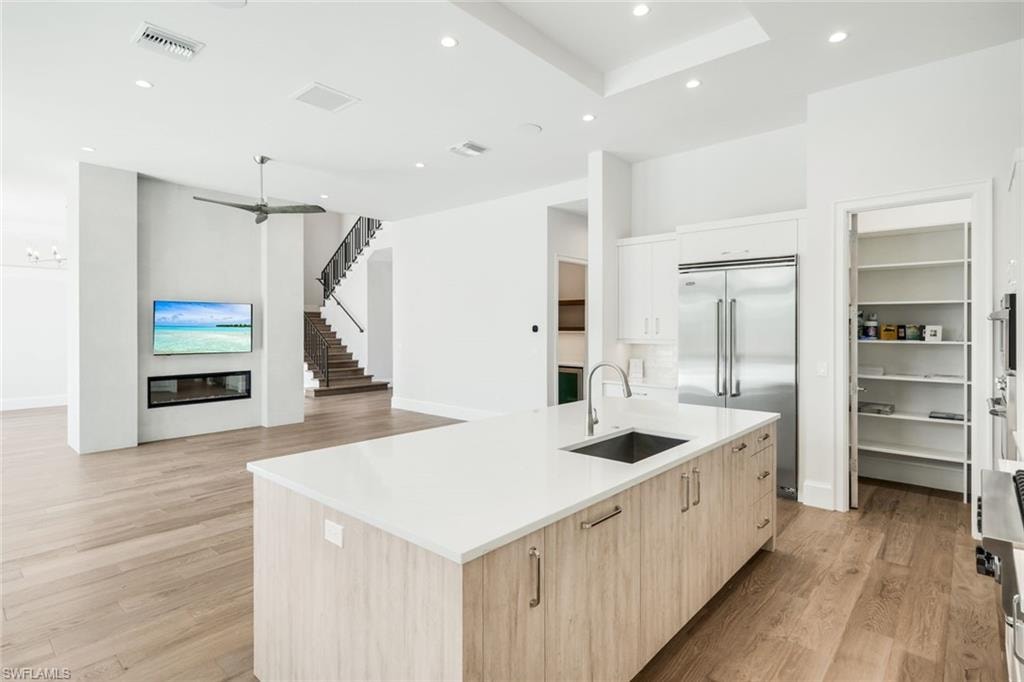 Two tone kitchen with a kitchen island with sink, light wood-type flooring, stainless steel appliances, modern cabinets, and recessed lighting