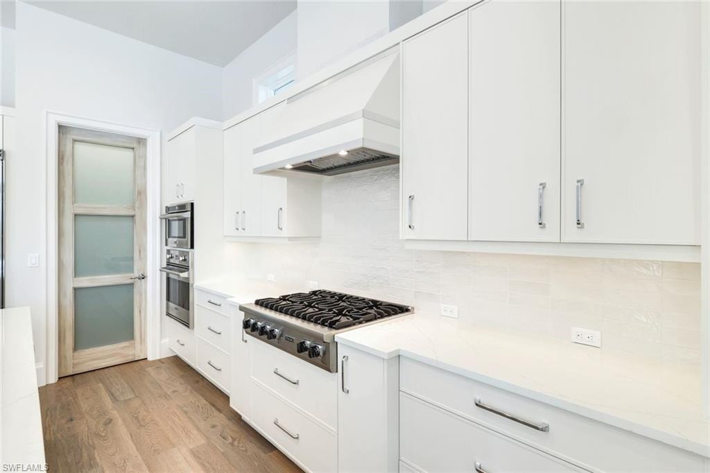 Kitchen featuring white cabinetry, stainless steel appliances, light wood-style floors, and decorative backsplash