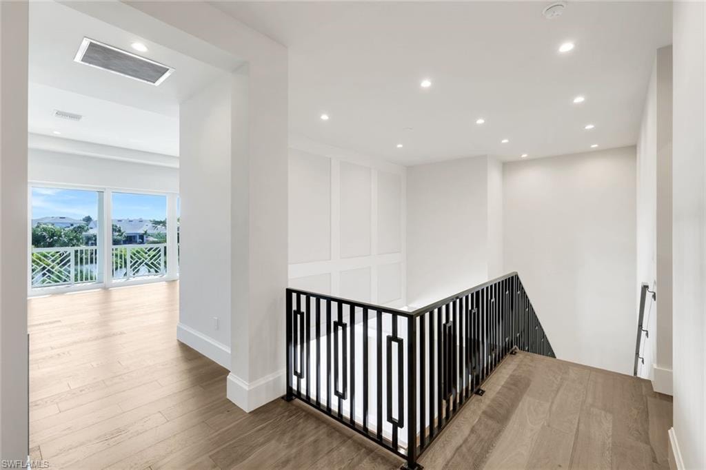 Corridor with an upstairs landing, wood finished floors, and recessed lighting