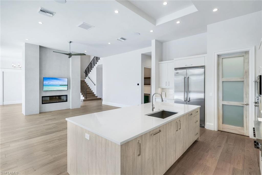 Kitchen with a kitchen island with sink, light wood finished floors, stainless steel built in refrigerator, light wood finish cabinetry, and recessed lighting
