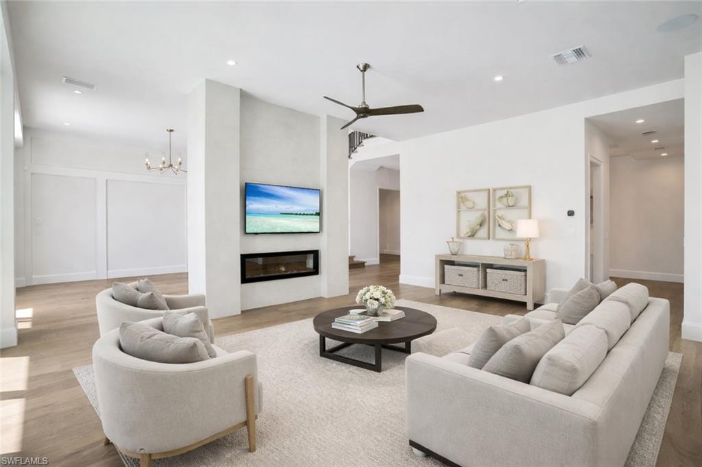 Living area with a glass covered fireplace, light wood-style floors, ceiling fan, and a chandelier