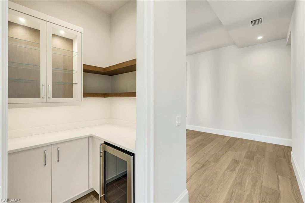 Bar area featuring recessed lighting, beverage cooler, light wood-style flooring, light countertops, and white cabinetry