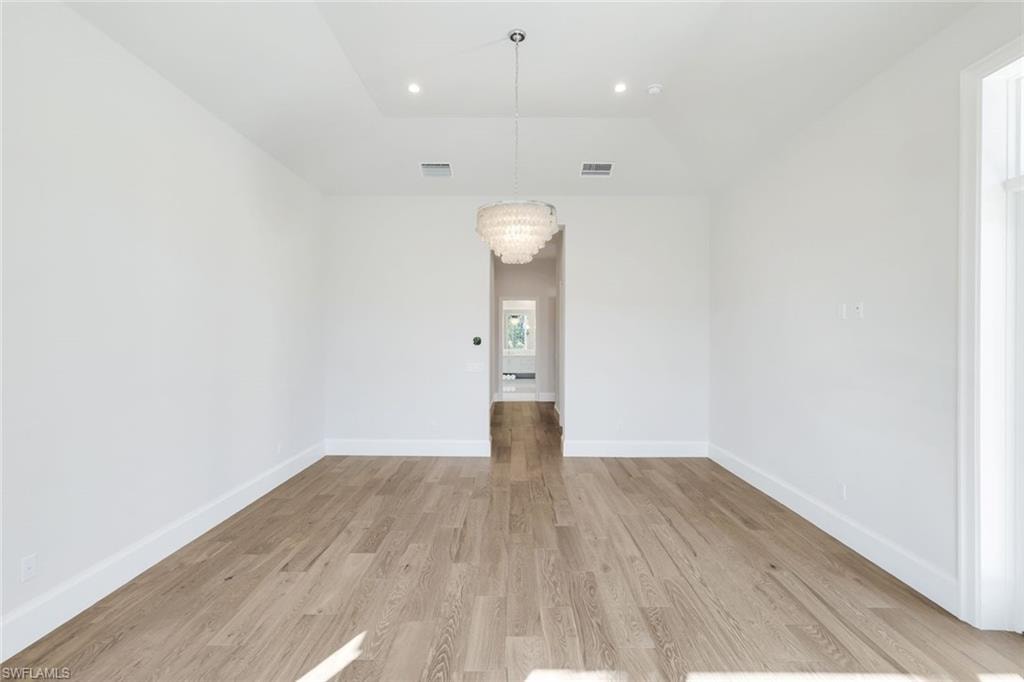 Unfurnished room with hanging lights, light wood-style floors, and lofted ceiling