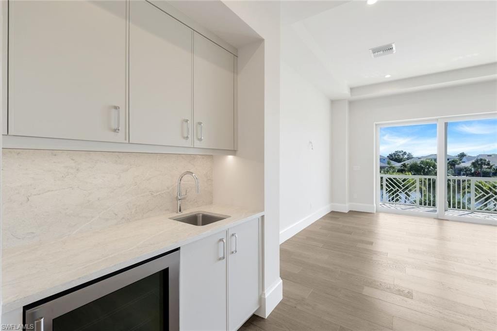 Indoor wet bar with beverage cooler, light stone counters, light wood-type flooring, recessed lighting, and tasteful backsplash