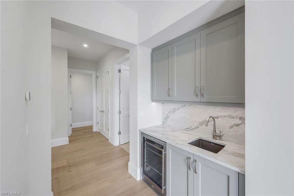 Indoor wet bar featuring gray cabinets, light stone counters, beverage cooler, light wood-style floors, and recessed lighting