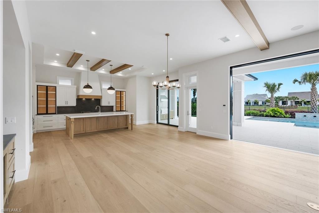 Kitchen featuring beam ceiling, two tone cabinetry, a large island with sink, open floor plan, and light wood finished floors