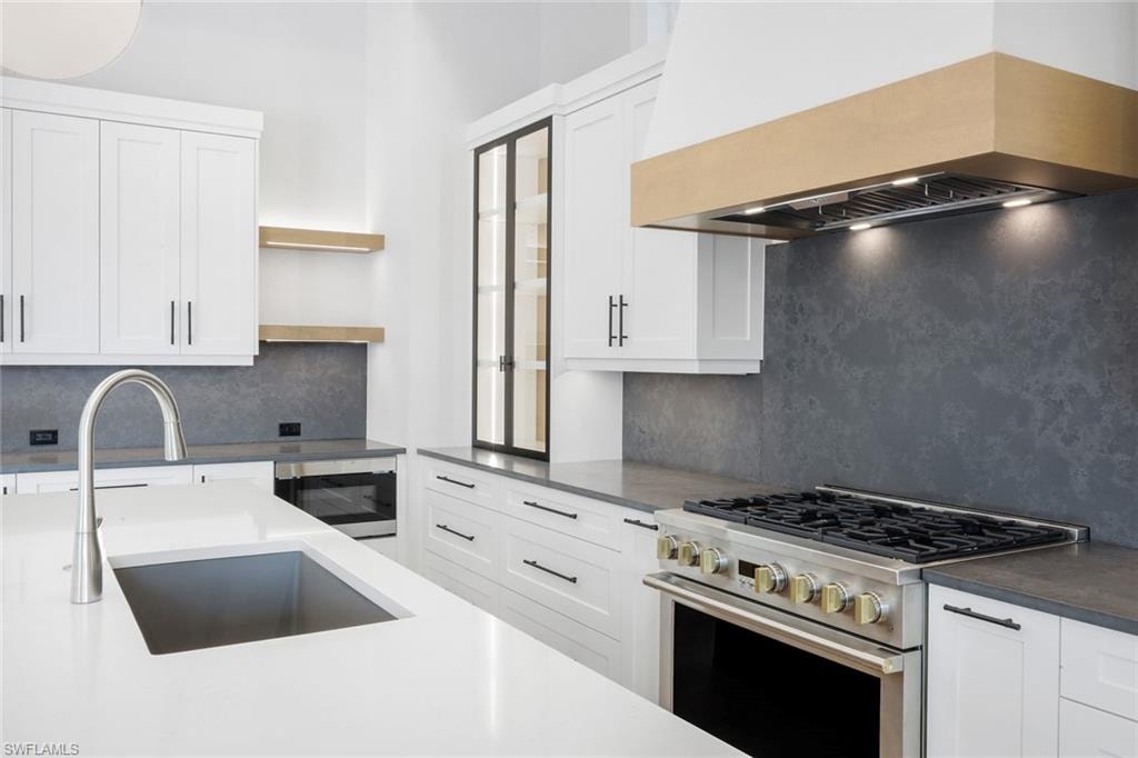 Kitchen featuring stainless steel appliances, white cabinets, tasteful backsplash, open shelves, and dark stone counters