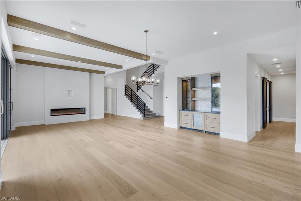 Unfurnished living room with recessed lighting, beamed ceiling, light wood finished floors, and a glass covered fireplace