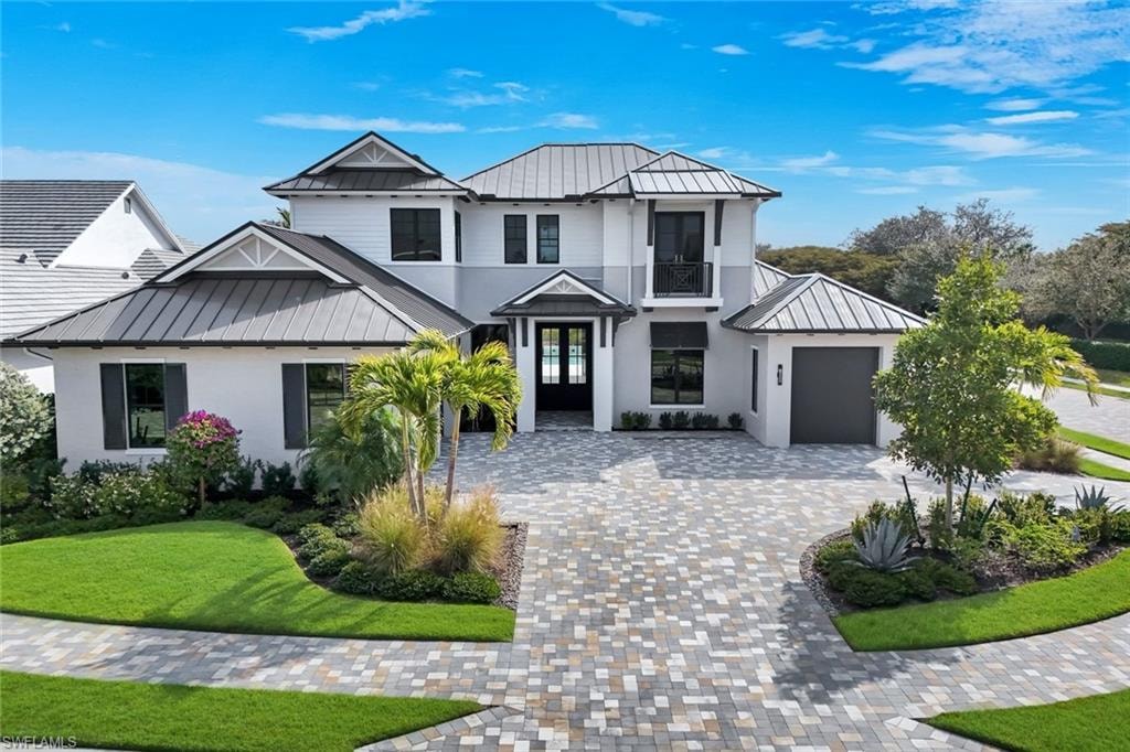 View of front of home featuring a standing seam roof, an attached garage, a front yard, decorative driveway, and stucco siding