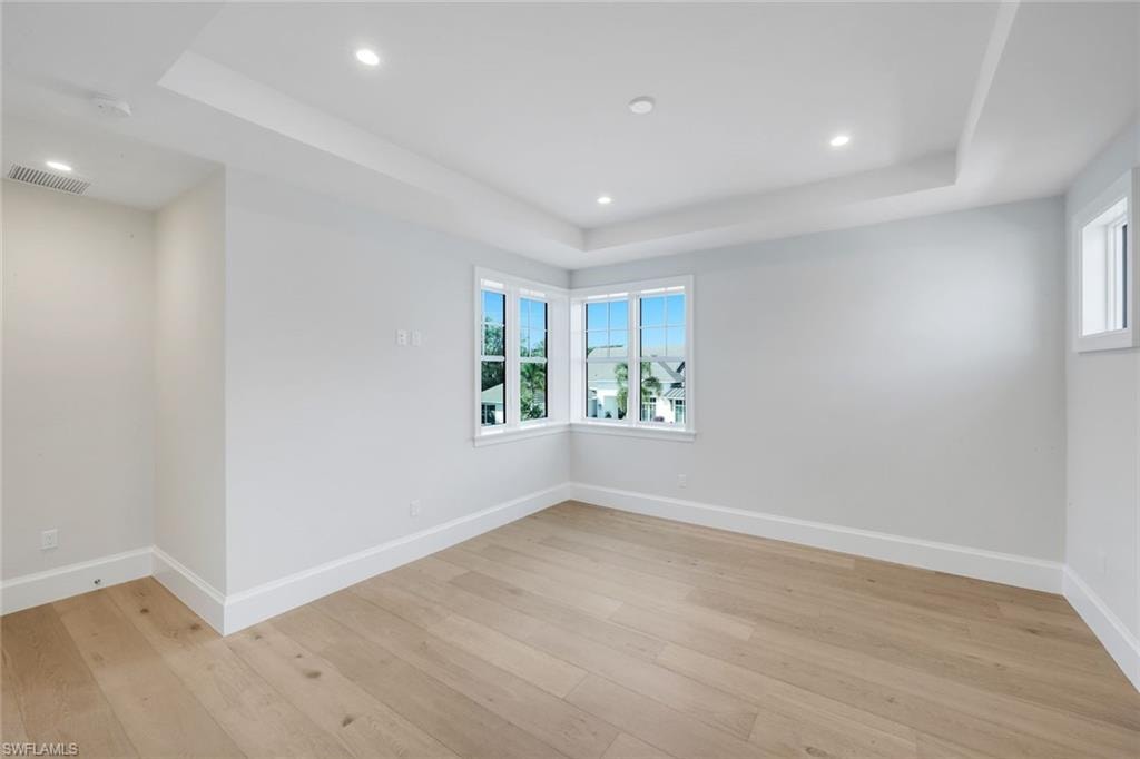 Spare room with a tray ceiling, plenty of natural light, recessed lighting, and light wood-style floors