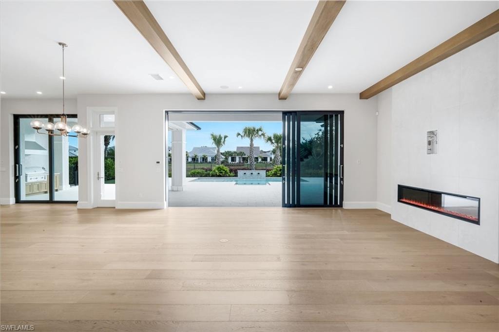 Unfurnished living room featuring light wood-type flooring, a tiled fireplace, beam ceiling, and a chandelier