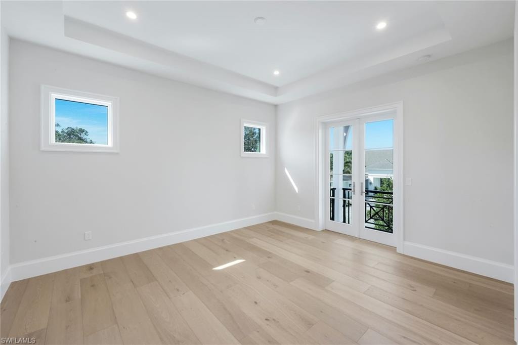 Empty room featuring light wood-type flooring, french doors, recessed lighting, and a tray ceiling