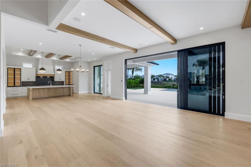 Unfurnished living room featuring beamed ceiling, a chandelier, and light wood-style floors