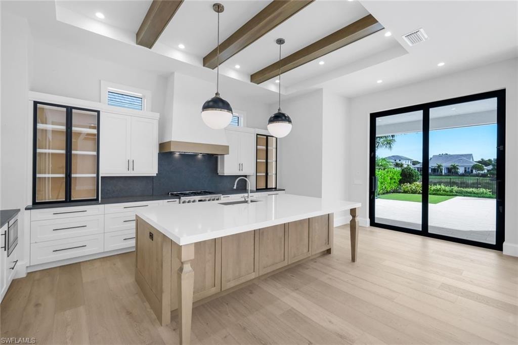 Two tone kitchen featuring beam ceiling, dual tone cabinetry, decorative light fixtures, a spacious island, and tasteful backsplash