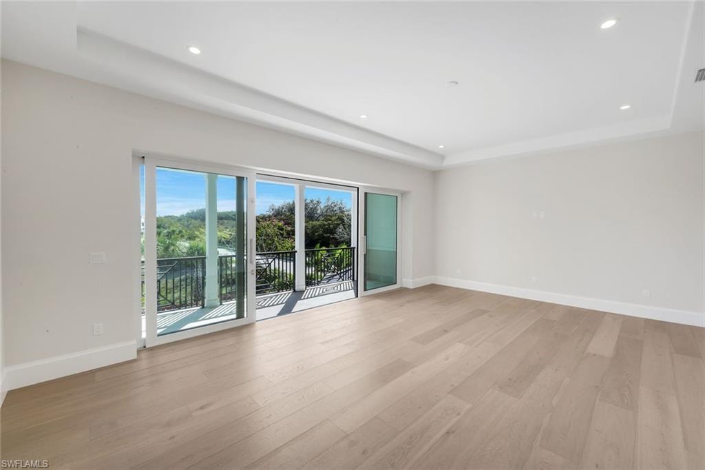Empty room featuring a raised ceiling, light wood-style floors, and recessed lighting
