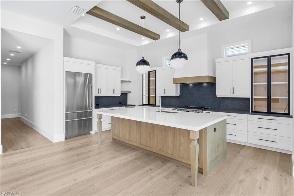 Two tone kitchen featuring two tone color scheme, high quality fridge, pendant lighting, decorative backsplash, and a large island with sink