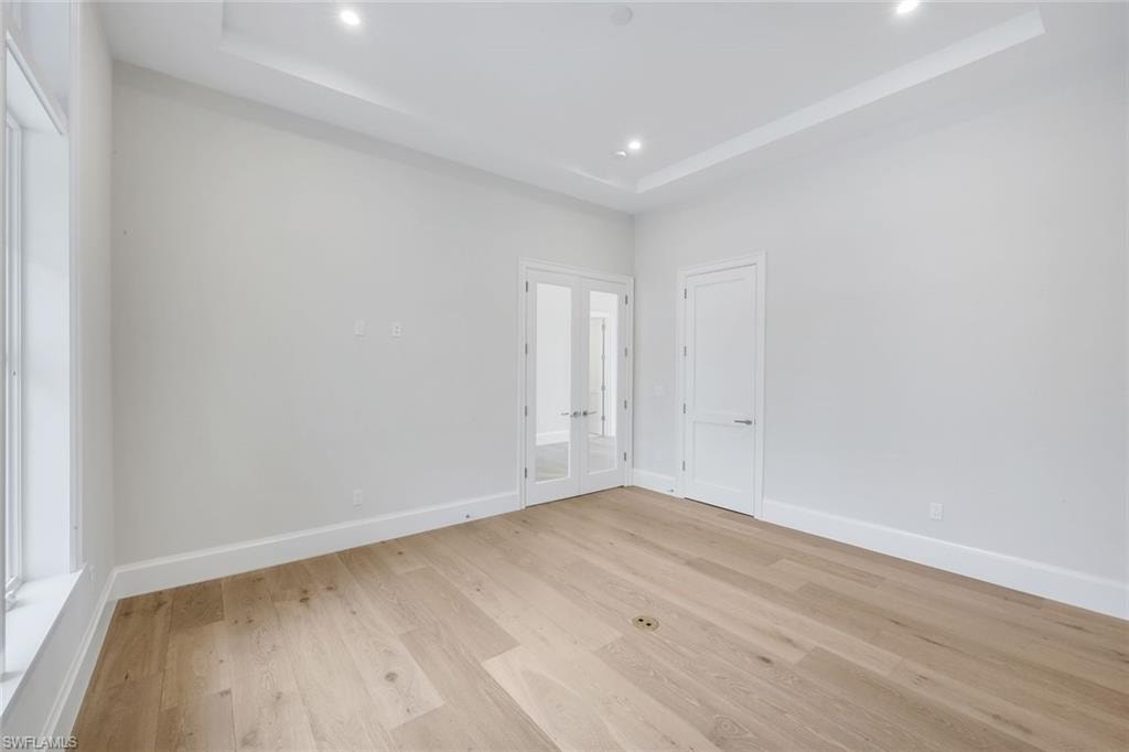 Unfurnished bedroom featuring a tray ceiling, french doors, light wood-style floors, and recessed lighting