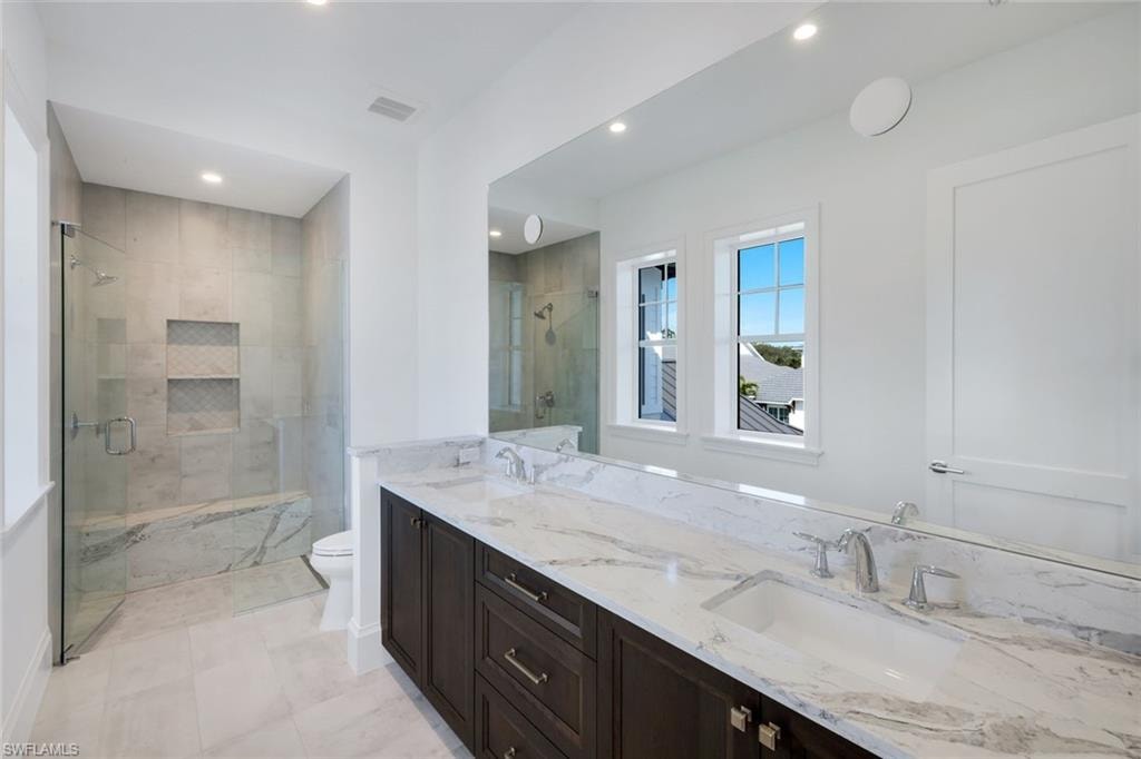 Full bath featuring a marble finish shower, double vanity, and recessed lighting