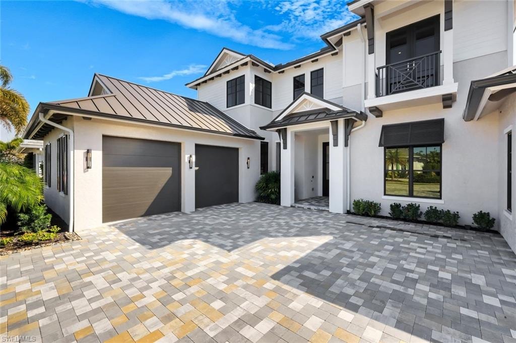 View of front of house with a standing seam roof, decorative driveway, stucco siding, and a balcony