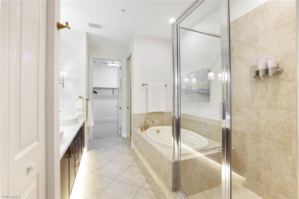 Full bathroom with a spacious closet, vanity, a bath, a stall shower, and light tile patterned floors