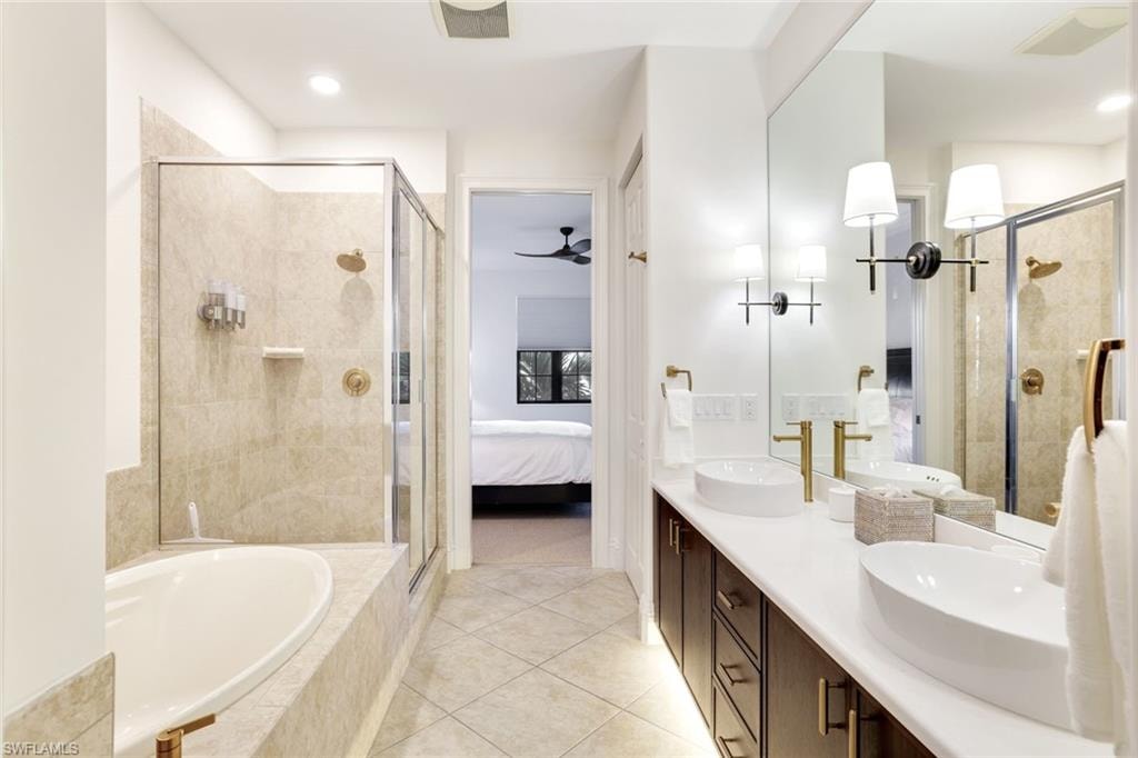 Full bathroom featuring connected bathroom, a stall shower, a garden tub, double vanity, and ceiling fan