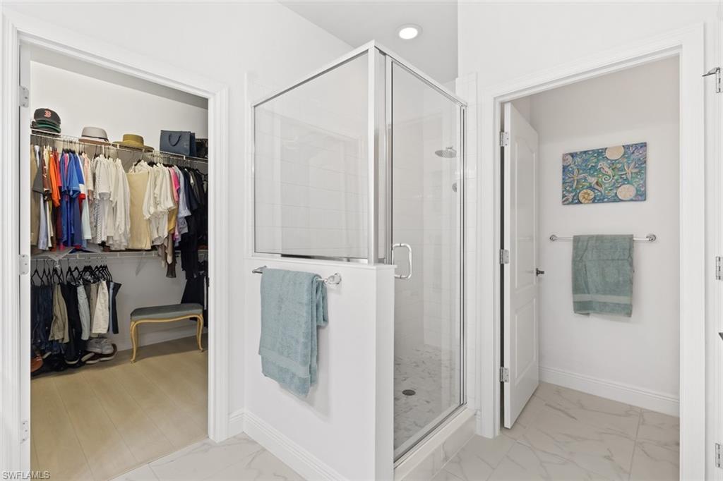 Full bathroom featuring a stall shower, a spacious closet, and light marble finish floors