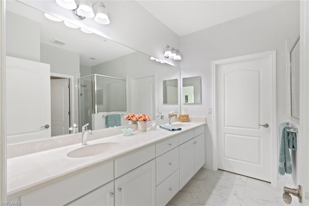 Full bath featuring a shower stall, double vanity, and light marble finish flooring