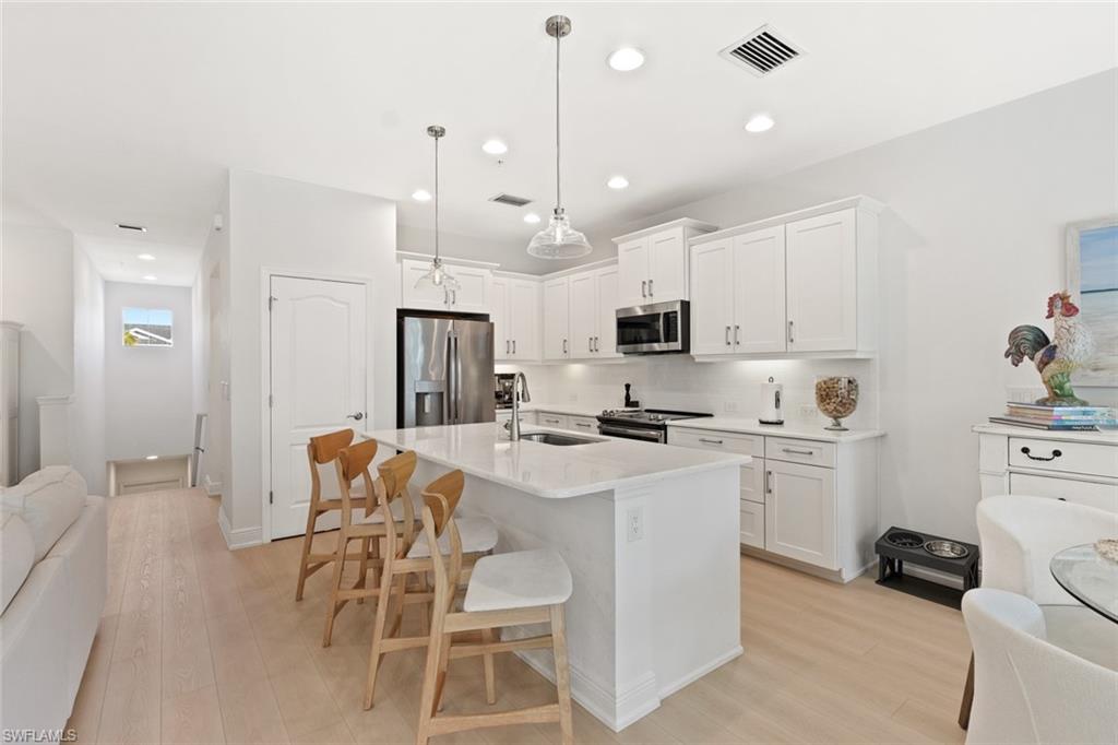 Kitchen featuring open floor plan, appliances with stainless steel finishes, a kitchen bar, white cabinets, and light wood finished floors
