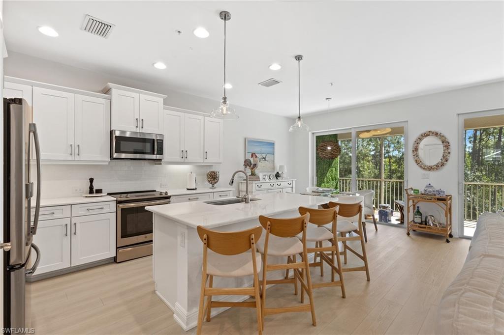 Kitchen with stainless steel appliances, a kitchen bar, pendant lighting, white cabinetry, and an island with sink