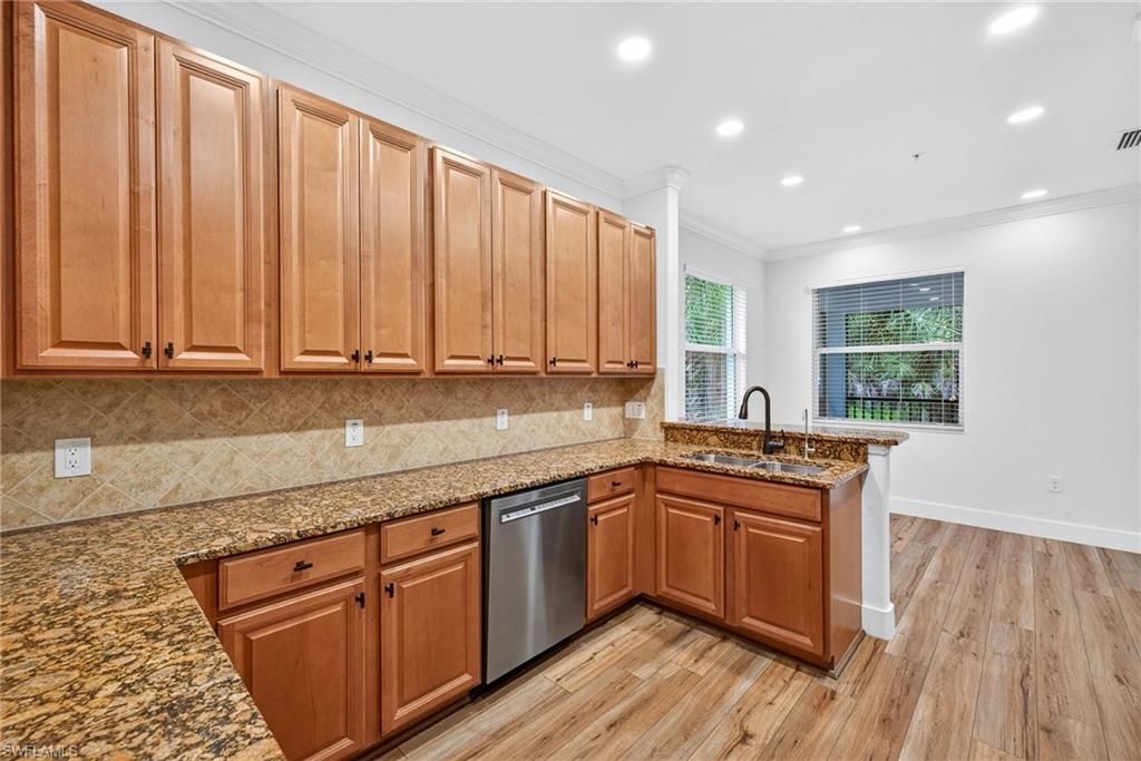 Kitchen featuring dark stone countertops, crown molding, decorative backsplash, light wood-style flooring, and recessed lighting