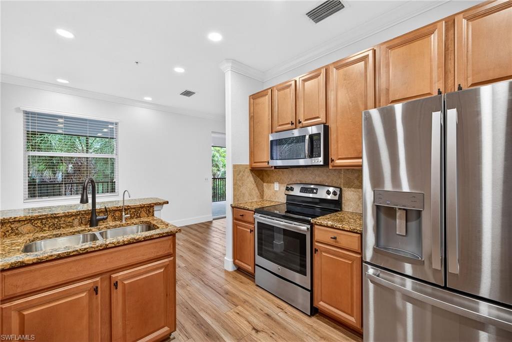 Kitchen with stainless steel appliances, light stone counters, light wood-style floors, crown molding, and recessed lighting
