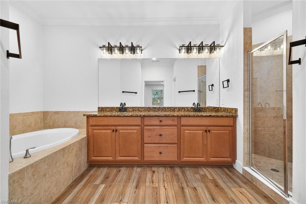 Full bathroom with a stall shower, double vanity, light wood-type flooring, ornamental molding, and a garden tub