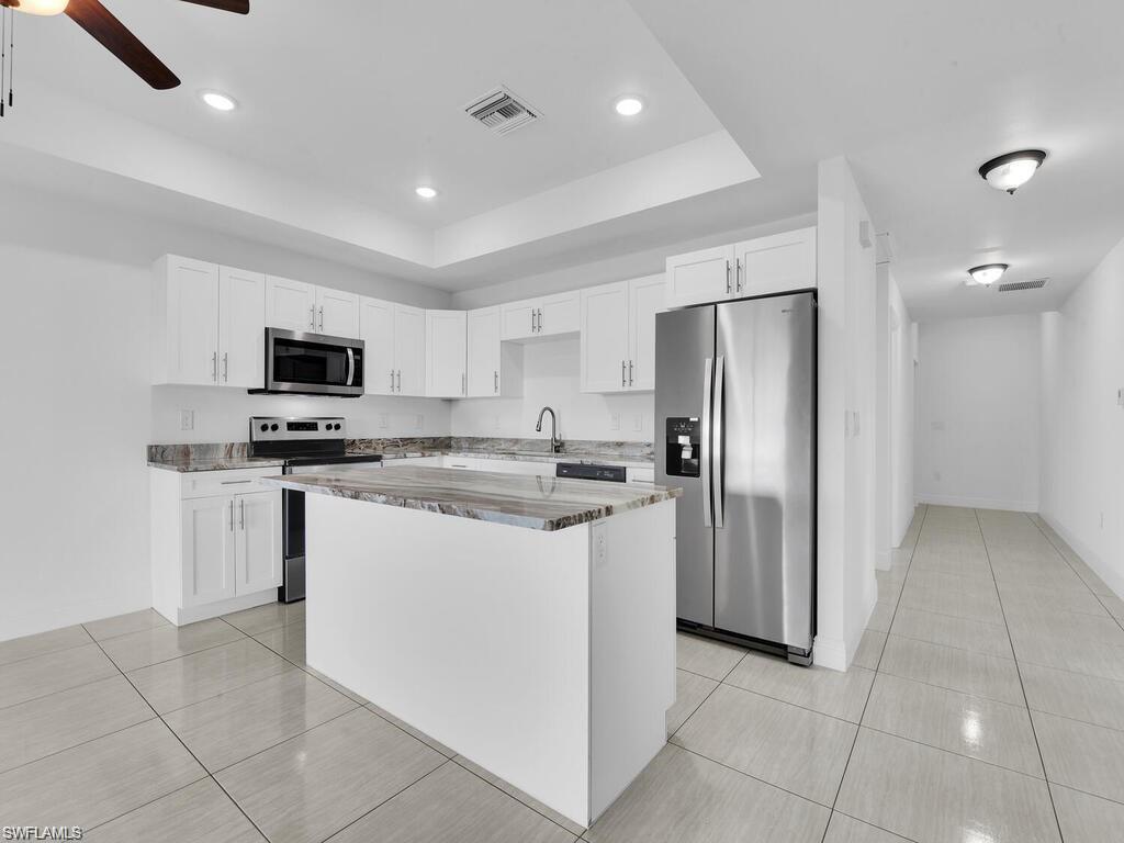 Kitchen with stainless steel appliances, white cabinets, light tile patterned floors, light stone counters, and recessed lighting
