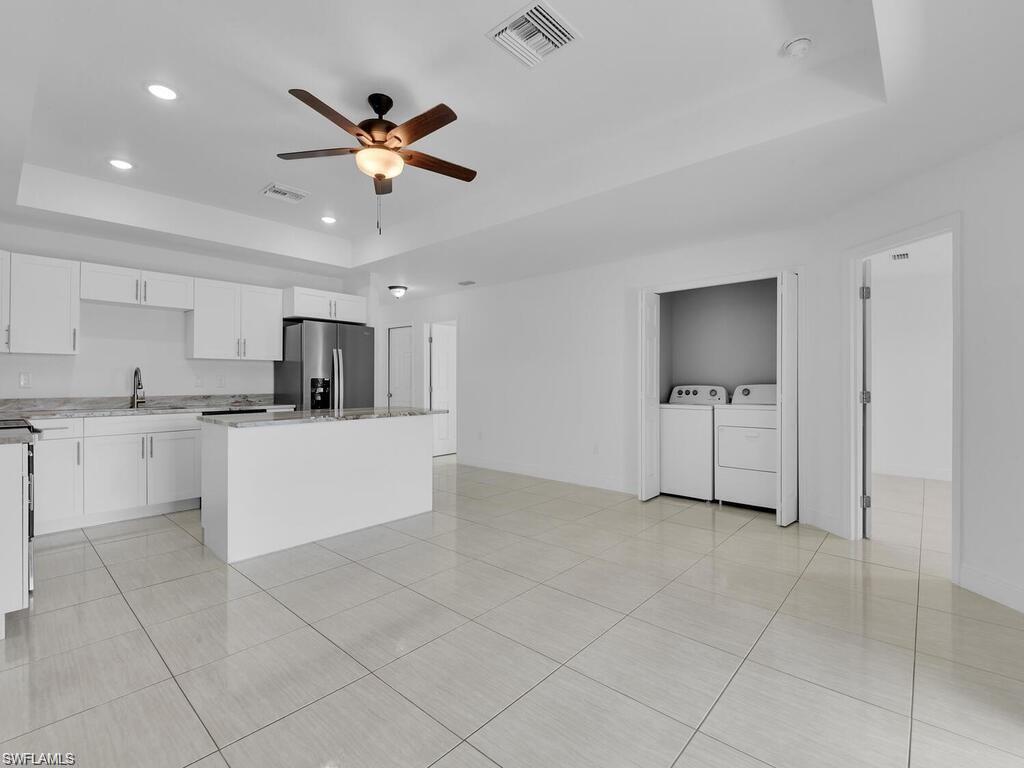 Kitchen featuring a tray ceiling, white cabinetry, recessed lighting, stainless steel refrigerator with ice dispenser, and light tile patterned floors