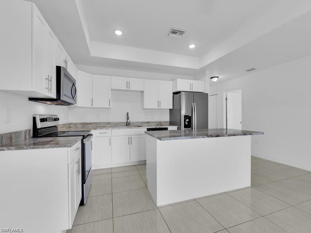 Kitchen with stainless steel appliances, white cabinetry, a center island, a tray ceiling, and recessed lighting