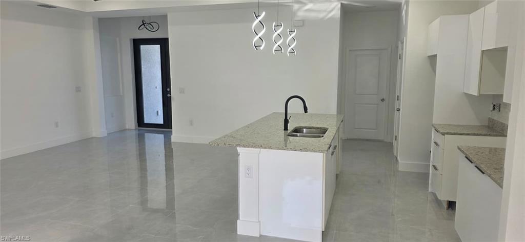 Kitchen featuring white cabinetry, light stone counters, a kitchen island with sink, and decorative light fixtures