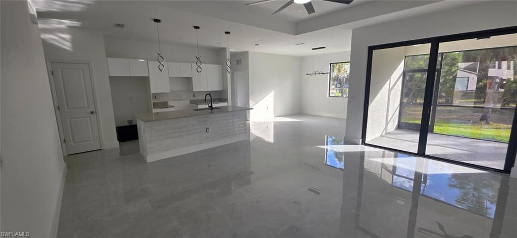 Kitchen featuring white cabinets, light stone countertops, a kitchen island with sink, pendant lighting, and a ceiling fan
